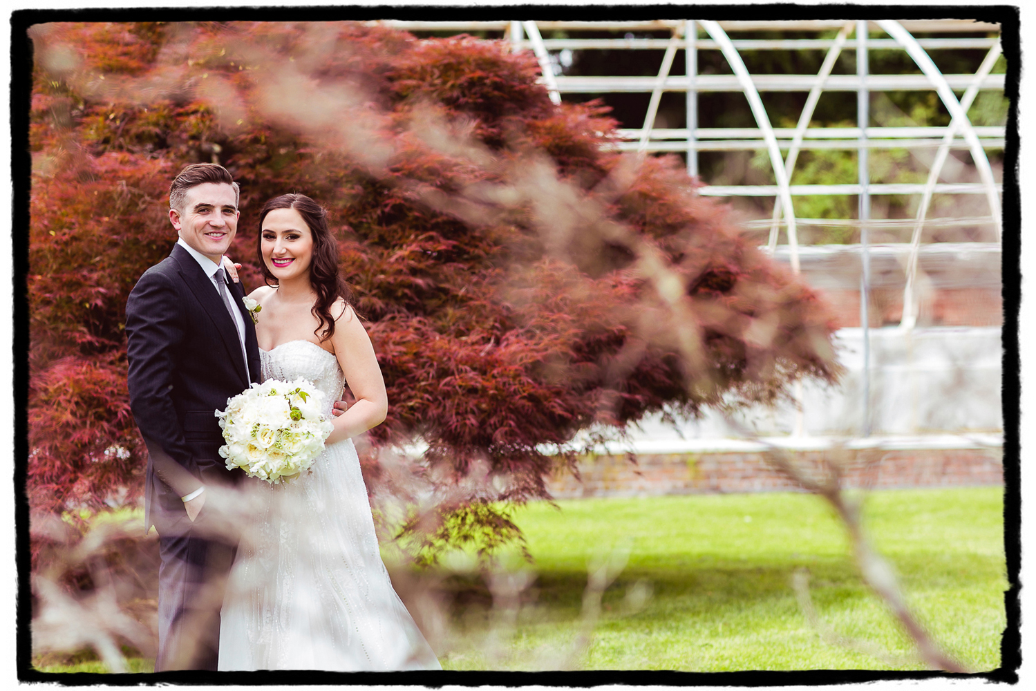 I love shooting through foliage, or in this case creating a nice blurry bokeh in the foreground wtih some branches framing the couple on the left.  The red maple behind them makes them pop and I loved the graphic lines in the greenhouse to the right.